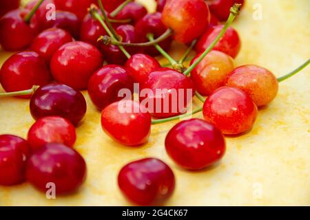 Primo piano di ciliegie rosse mature su sfondo giallo, vista orizzontale, messa a fuoco selettiva. Foto Stock