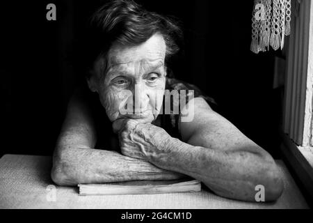 Una donna anziana si siede pensierosamente a casa sua. Foto in bianco e nero. Foto Stock