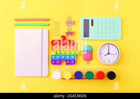 Posa piatta di cancelleria, orologio e giocattoli in silicone popit su sfondo giallo Foto Stock