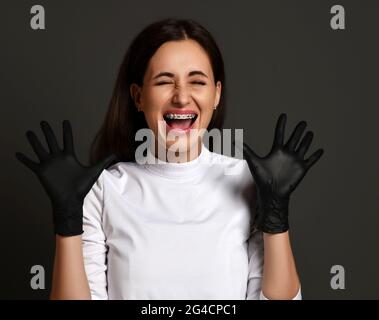 Ritratto di giovane donna allegra e sorridente dentista medico in uniforme bianca, guanti in lattice che mostrano le sue parentesi graffe Foto Stock