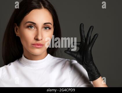 Ritratto di giovane donna attraente dentista medico in uniforme bianca e guanti in lattice che mostrano ok buon segno Foto Stock