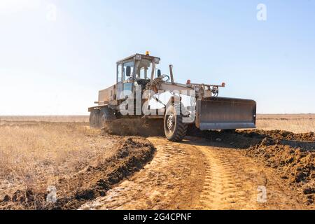 macchina livellatrice che fa una nuova strada, scavare la ghiaia sporcizia nel campo Foto Stock