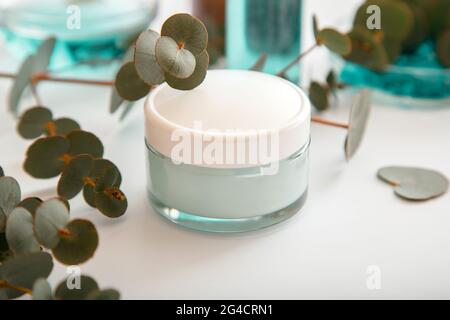 Crema idratante in vaso di vetro con foglie di eucalipto. Set di cosmetici per la cura della pelle all'eucalipto in confezione bianca mockup su sfondo bianco. Naturale Foto Stock