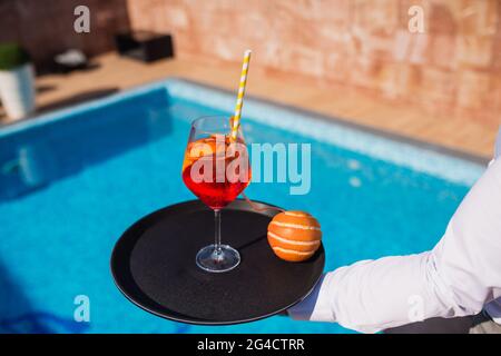 Il barman serve cocktail e arancio in un resort di lusso vicino alla piscina. Festa calda estiva Foto Stock