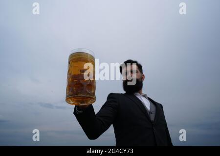 Uomo che beve birra su sfondo cielo. Buon birraio con bicchiere di birra. Foto Stock