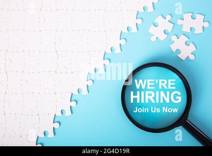 Puzzle bianco con parola che stiamo assumendo su sfondo blu. Concetto di reclutamento Foto Stock