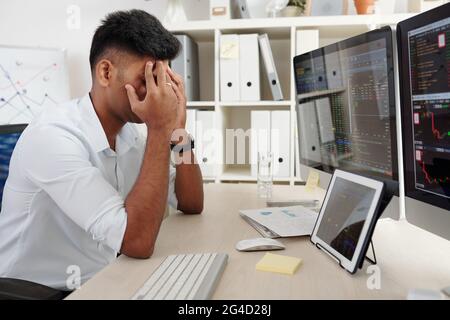 Intermediario di mercato azionario che copre gli occhi con le mani quando si siede al tavolo stressato dopo aver perso un sacco di soldi Foto Stock