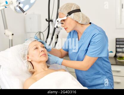 Professional cosmetico esaminando la pelle del viso di donna matura in clinica di estetica cosmetologia Foto Stock