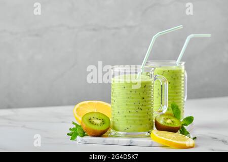 Due bicchieri con kiwi e frullato al limone con menta su sfondo marmoreo e fette di frutta Foto Stock