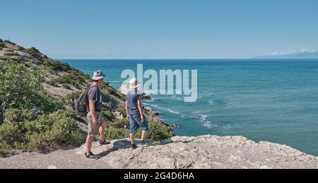 Un ragazzo e suo nonno in piedi sulla costa rocciosa del mare, guardando il paesaggio. Concetto di viaggio locale. Foto Stock