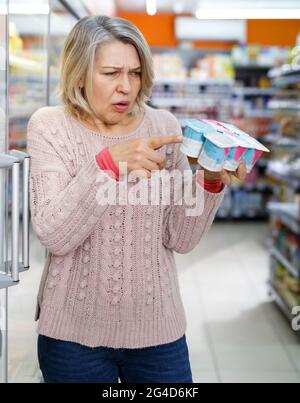 Donna bionda stupita che legge i contenuti dei prodotti Foto Stock