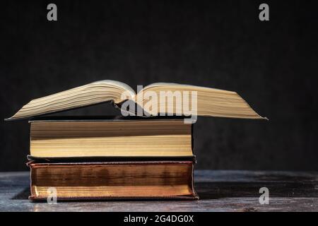 Una pila di vecchi libri che giace su un tavolo su uno sfondo scuro Foto Stock