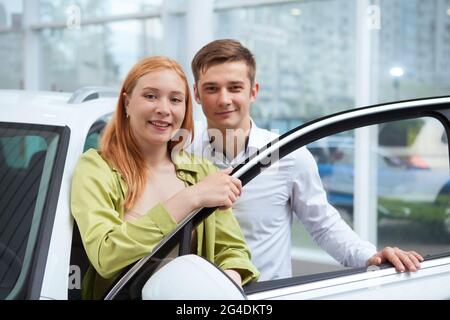 Felice coppia sorridente alla macchina fotografica, scegliendo nuova automobile da comprare insieme alla concessionaria Foto Stock