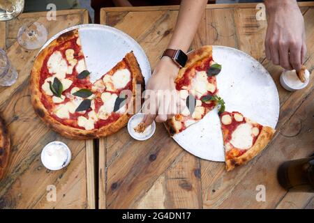 Vista dall'alto di amici anonimi che si tuffano pezzi di pizza in salsa mentre si cena insieme durante la festa Foto Stock