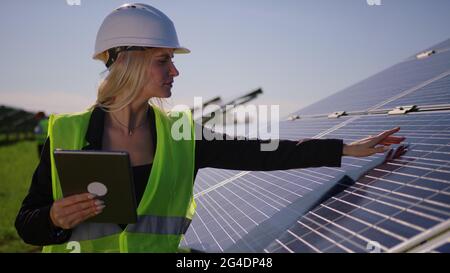 L'ingegnere ecologico femminile utilizza tablet digitali e raccoglie informazioni efficienti sui pannelli solari. Fotovoltaico solare fattoria. Energia verde Foto Stock