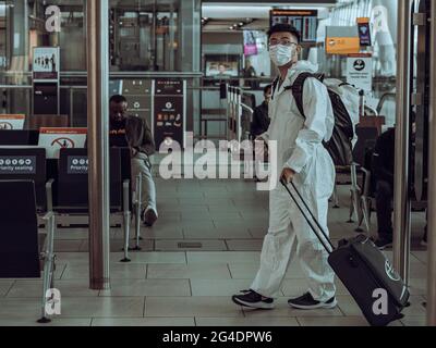 Un viaggiatore in completo DPI cammina in un terminal dell'aeroporto. Il passeggero vestito con una tuta di protezione completa attraversa il terminal passeggeri Foto Stock