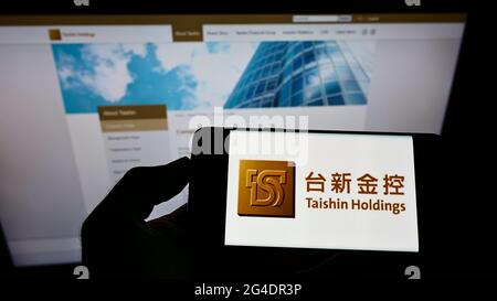 Persona che detiene smartphone con il logo della società taiwanese Taishin Financial Holding Co. Ltd. Sullo schermo di fronte al sito web. Mettere a fuoco il display del telefono. Foto Stock