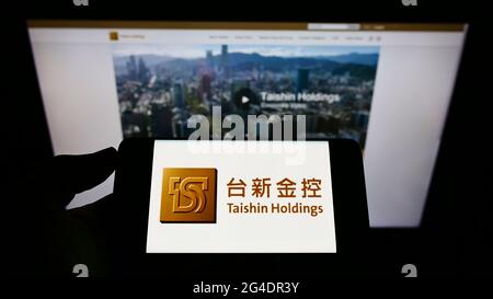Persona che tiene il telefono monbile con il logo della società taiwanese Taishin Financial Holding sullo schermo davanti alla pagina web. Mettere a fuoco il display del telefono. Foto Stock