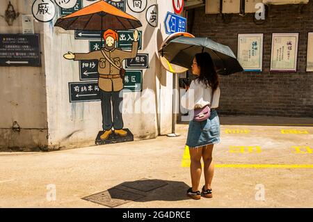 Un visitatore del quartiere artistico M50 al riparo dal sole di fronte al lavoro d'arte su un muro di un poliziotto Sikh Putuo District, Shanghai, Cina. Foto Stock