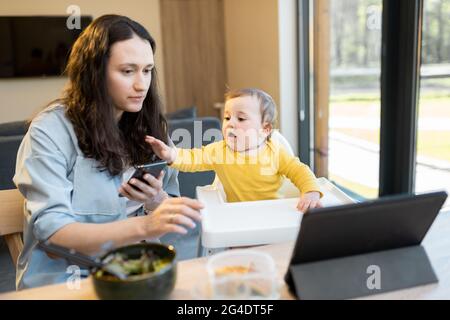 Bambino e genitori impegnati in un gadget digitale durante un pranzo a casa Foto Stock