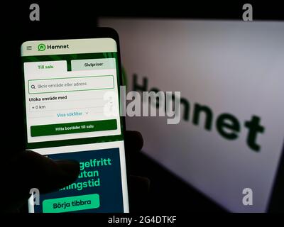 Persona che detiene smartphone con il sito web della società svedese di piattaforma Hemnet AB sullo schermo di fronte al logo. Mettere a fuoco il centro del display del telefono. Foto Stock