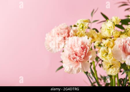 Bouquet di garofani rosa e mattiola gialla con rami verdi. Design concetto di saluto per le vacanze con bouquet di garofano su sfondo rosa. Foto Stock