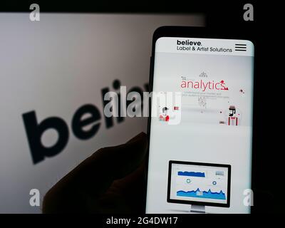 Persona che tiene il cellulare con la pagina web dell'etichetta francese del disco credo digitale sullo schermo di fronte al logo dell'azienda. Mettere a fuoco il centro del display del telefono. Foto Stock