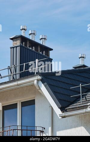 Vista ravvicinata del tubo in pietra di mattoni coperto di lamiere e una scatola nera di fumo sul tetto. Tubo di ventilazione sul tetto della casa moderna Foto Stock