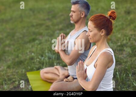 Donna e uomo seduti in posizione loto con gli occhi chiusi, meditando e praticando yoga sulla natura Foto Stock