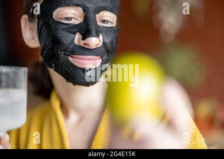 Ritratto di una giovane donna in maschera di pulizia nera sul viso con un bicchiere d'acqua Foto Stock