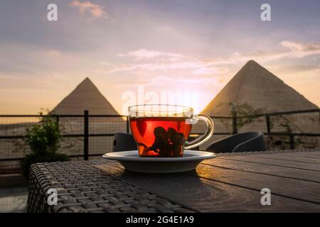 Tè arabo tradizionale in un bicchiere sullo sfondo delle grandi piramidi di Giza. Bella vista dell'attrazione nel ristorante al tramonto. Th Foto Stock