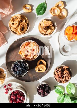 Vari frutti secchi e bacche. Disporre in ciotole su tavola bianca con ombre bacche secche o essiccate al sole. Spuntini naturali vegani sani. T Foto Stock