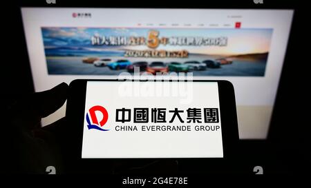 Persona che detiene smartphone con il logo della società di proprietà cinese Evergrande Real Estate Group sullo schermo di fronte al sito web. Mettere a fuoco il display del telefono. Foto Stock