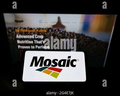 Persona che tiene il telefono mobile con il logo del produttore americano di fertilizzante l'azienda Mosaic sullo schermo davanti alla pagina di Web di affari. Mettere a fuoco il display del telefono. Foto Stock