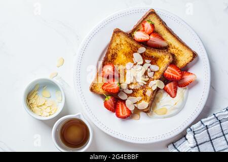 Toast alla francese con fragole, yogurt e sciroppo d'acero su piatto bianco, vista dall'alto. Concetto di colazione. Foto Stock