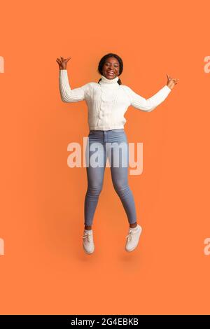Umore allegro. Happy Young Black Woman Jumpinmg in Air con mani sollevate Foto Stock