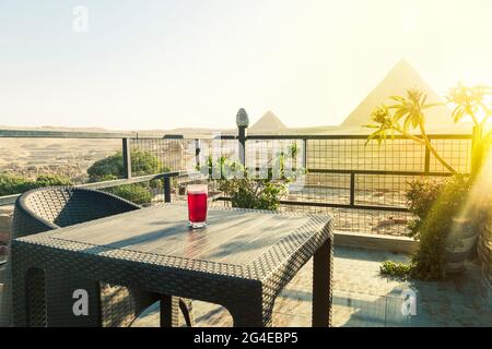 Tradizionale karkade arabo di tè alle erbe in un bicchiere sullo sfondo delle grandi piramidi di Giza. Bella vista dell'attrazione nel ristorante Foto Stock