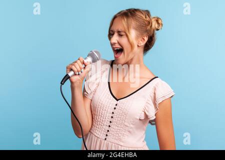 Profilo di giovane donna adulta che indossa abiti estivi cantando ad alta voce nel karaoke, donna di talento canta la canzone preferita nel microfono, mantiene gli occhi chiusi. IND Foto Stock