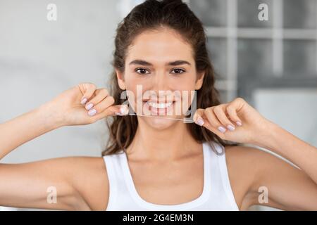 Happy Woman che tiene i denti Floss sorridente alla macchina fotografica nel bagno Foto Stock