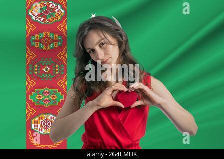 Amore Turkmenistan. Una ragazza tiene un cuore sul petto in mano sullo sfondo della bandiera del Turkmenistan. Il concetto di patriottismo. Foto Stock