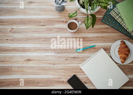 Tavolo con blocco note, libri, croissant e tazza di caffè, vista dall'alto Foto Stock