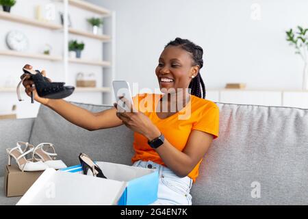 Felice donna nera che disimballa il pacco, facendo foto delle sue nuove  scarpe su smartphone per un feedback positivo del negozio online Foto stock  - Alamy