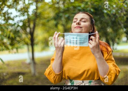 Felice ragazza toglie la sua maschera medica protettiva dal viso per respirare aria fresca dopo la fine della pandemia coronavirus Foto Stock