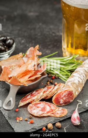 Set di antipasti di birra. Salsiccia di maiale affumicata su una tavola di ardesia e prosciutto secco a scatti. Spazio per il testo Foto Stock