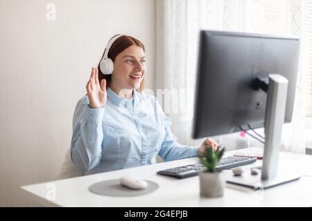 Buon responsabile caucasico con occhiali guardando lo schermo del computer, tenendo una piacevole conversazione con i clienti partner online, lavorando a distanza Foto Stock