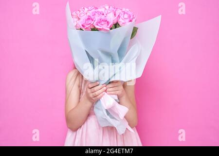 Una bambina in abito rosa con bouquet di rose, nascose dietro il flowers.The ragazza inala la fragranza di fiori su sfondo rosa Foto Stock