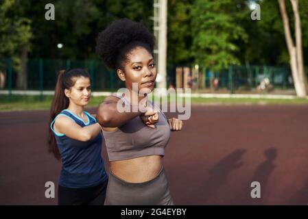 Due giovani donne sorridenti in forma che lavorano insieme in un parco facendo esercizio stretching e le estensioni delle mani per migliorare la flessibilità . Foto Stock