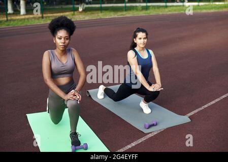 Due giovane donna sorridente in forma che lavora insieme in un parco facendo esercizio stretching e le estensioni delle gambe per migliorare la flessibilità. Foto Stock