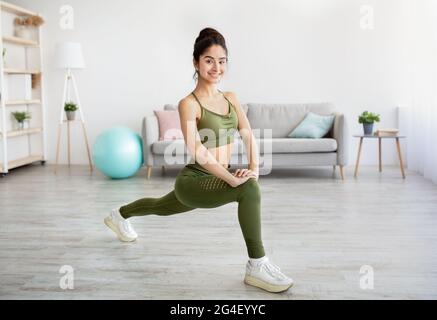Formazione domestica sulla quarantena. Attraente giovane signora indiana che fa affondo, che si esercita a casa, a lunghezza intera Foto Stock