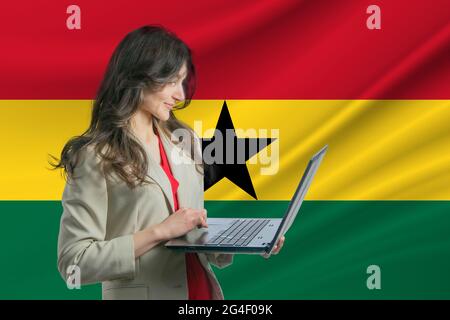 Freelance in Ghana. Bella giovane donna freelance utilizza il computer portatile sullo sfondo della bandiera del Ghana. Foto Stock